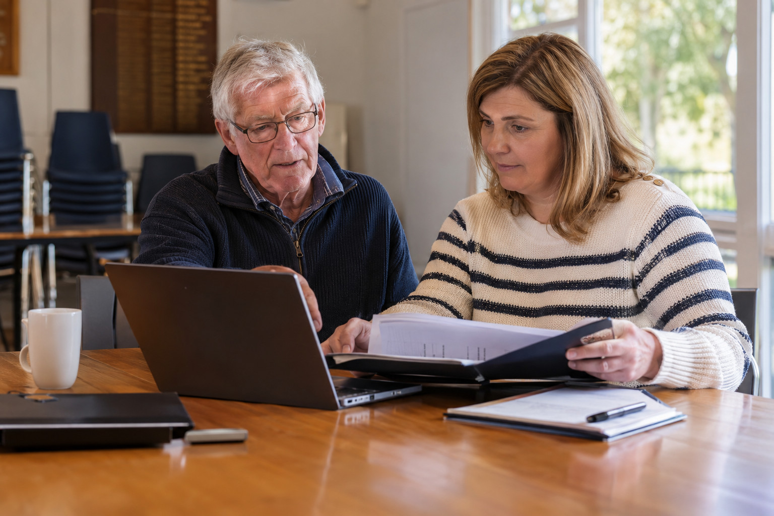 Two club committee members review account records during a website handover.