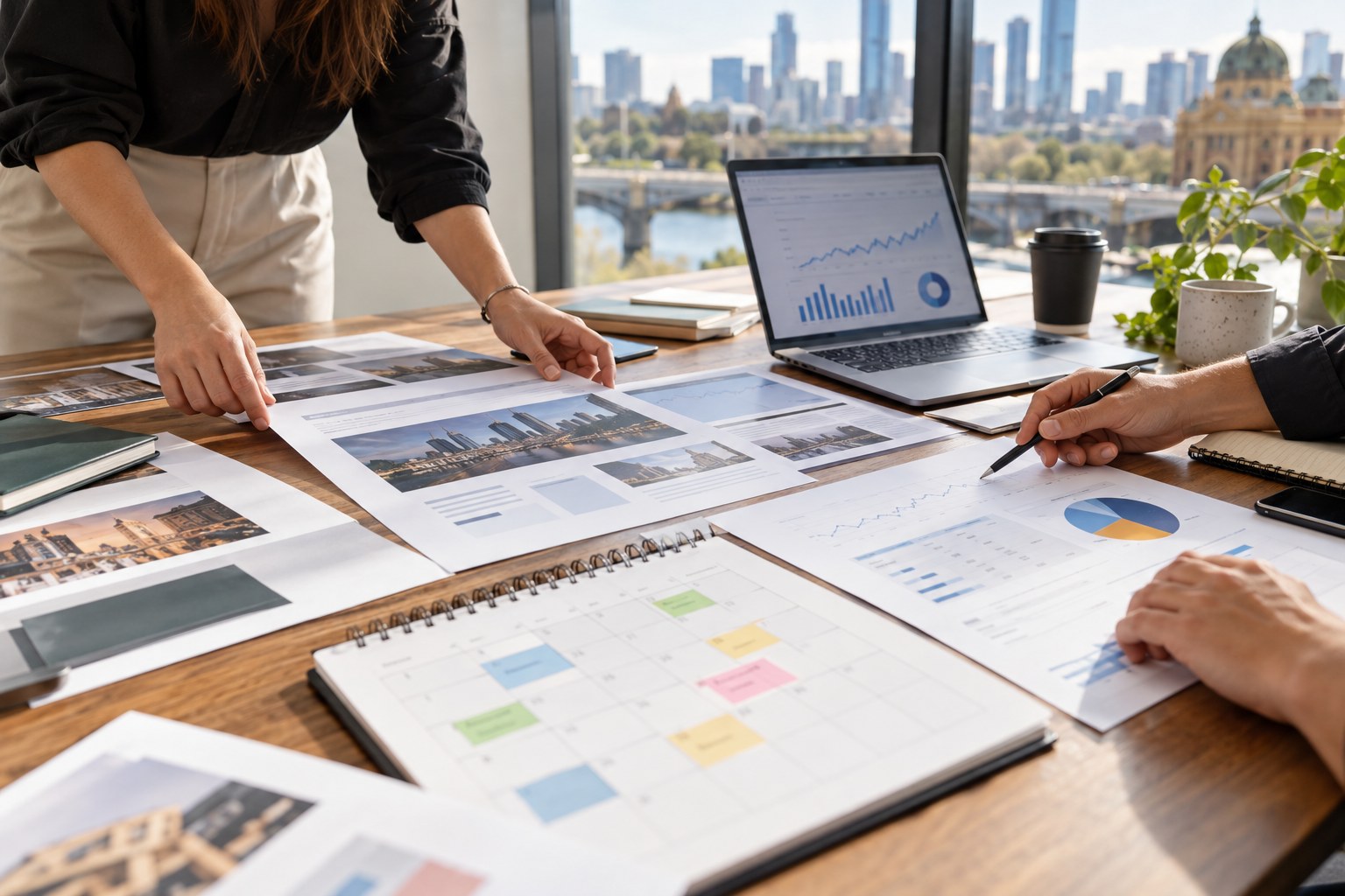 People review website printouts, a planning notebook and performance charts on a desk.